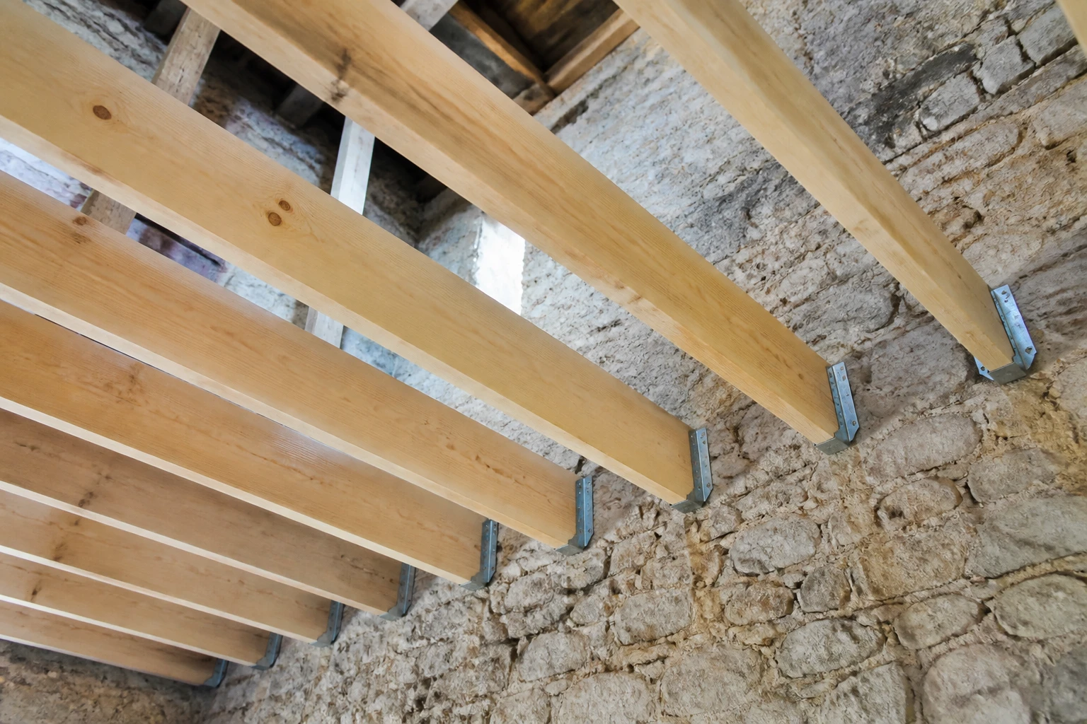 Solivage pour plafond en bois résineux avec sabots métalliques sur murs en pierre, chantier de rénovation