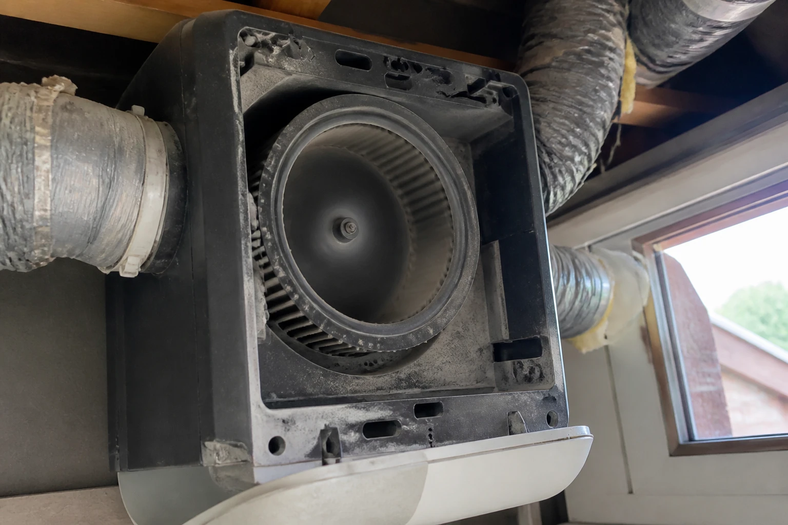 Caisson de VMC ouvert montrant la roue de ventilateur encrassée dans un faux-plafond de maison