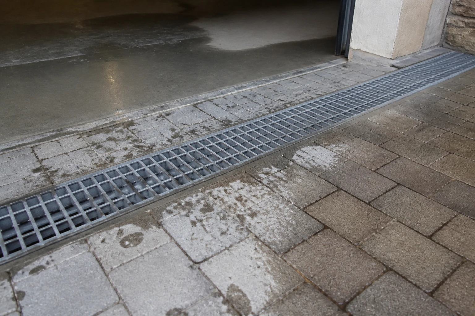 Caniveau eau pluviale avec grille métallique posé en travers d'une entrée de garage en pavés