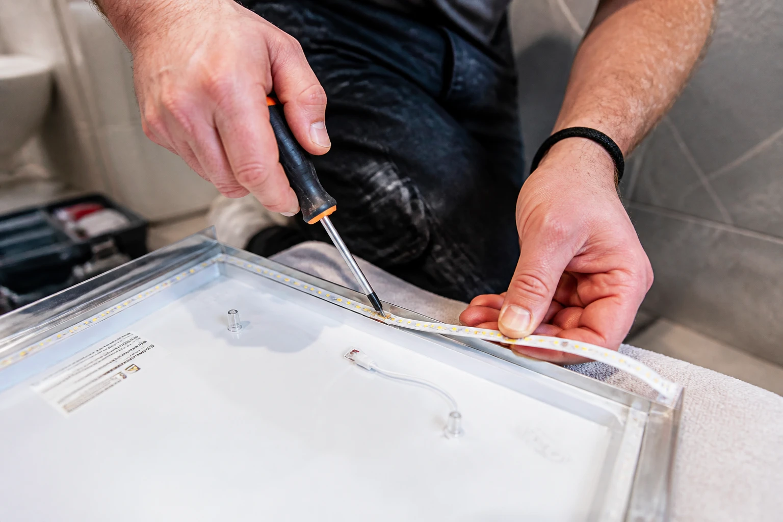 Artisan remplaçant un ruban LED à l'arrière d'un miroir de salle de bain démonté