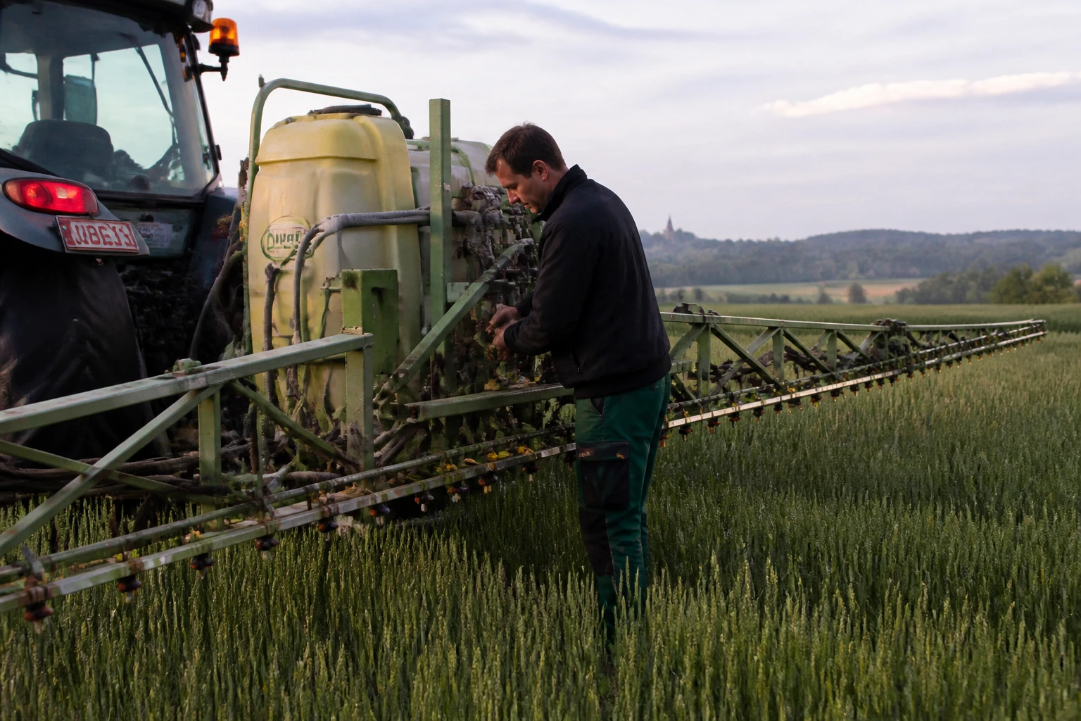 Agriculteur réglant un pulvérisateur tracteur en grandes cultures françaises, lumière matinale dorée